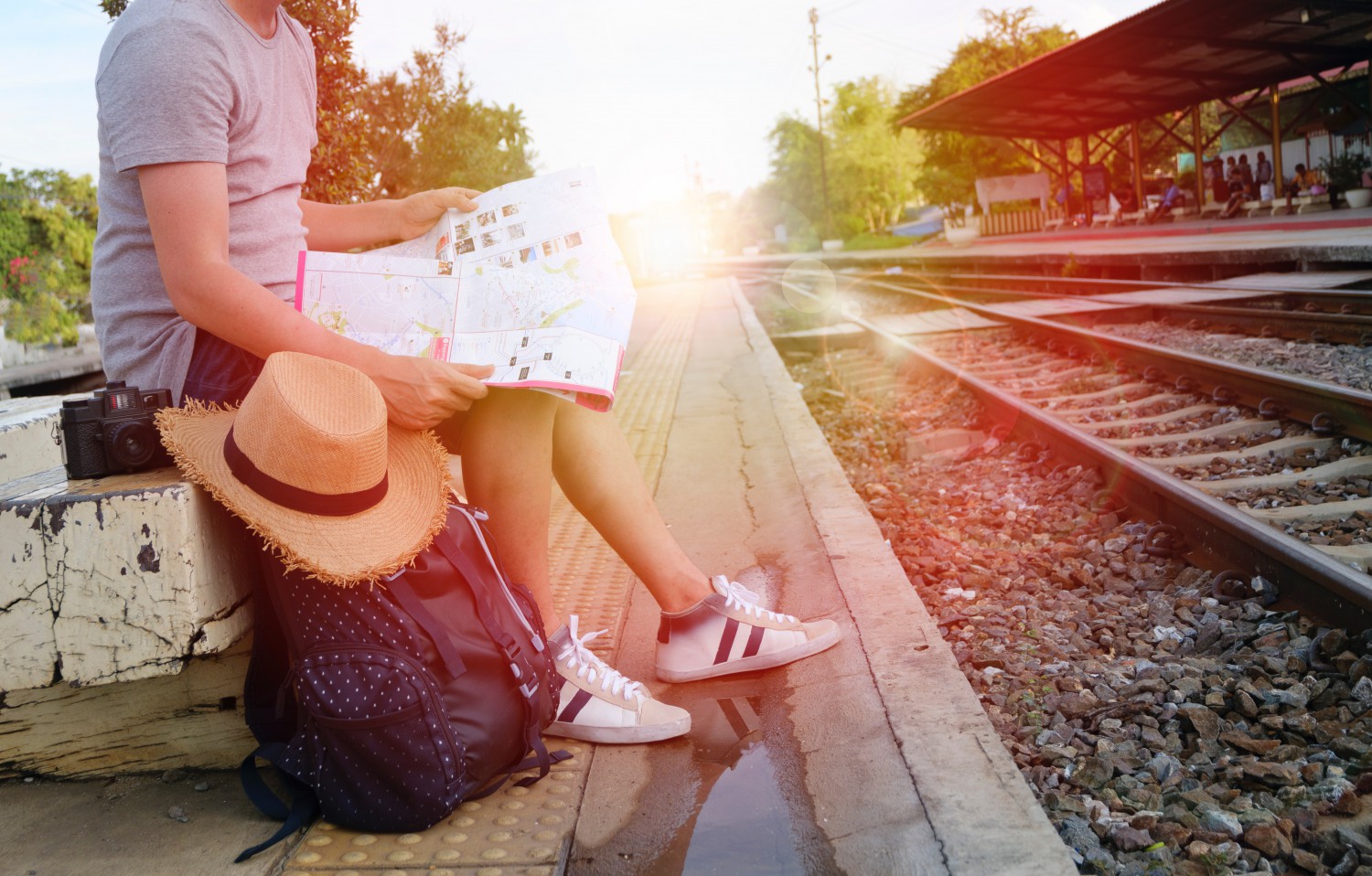 Traveler with a map, bag, and camera next to railway line