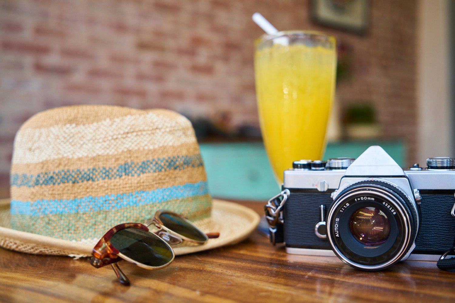 A hat, sunglasses, a glass of juice, and a camera on a table