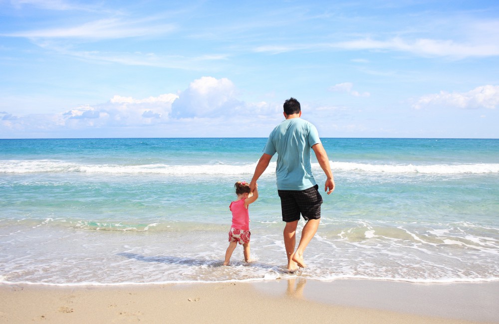 A man and a child walking on the beach while holding hands
